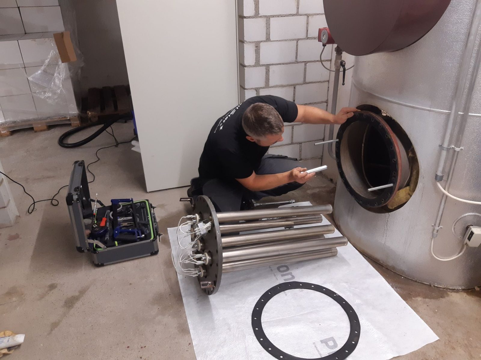 Servicetechniker arbeitet an der geöffneten Flanschöffnung eines Boilers, davor das ausgebaute Heizelement