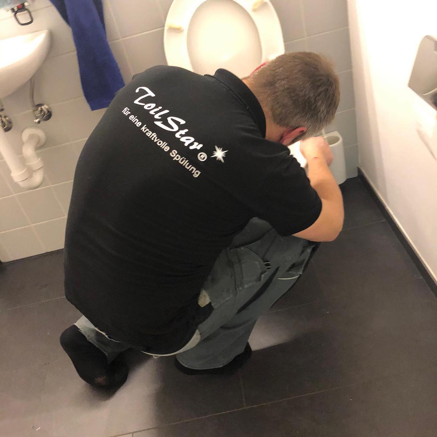 Servicetechniker von ToilStar kniet in einem Bad und arbeitet an einer WC-Anlage