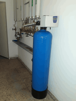 Blauer Enthärtungsbehälter an der Wand mit Anschlussarmatur und Rohrleitungen