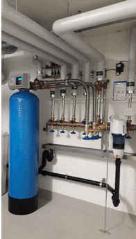 Hoher blauer Behälter einer Enthärtungsanlage neben der Wasserverteilung